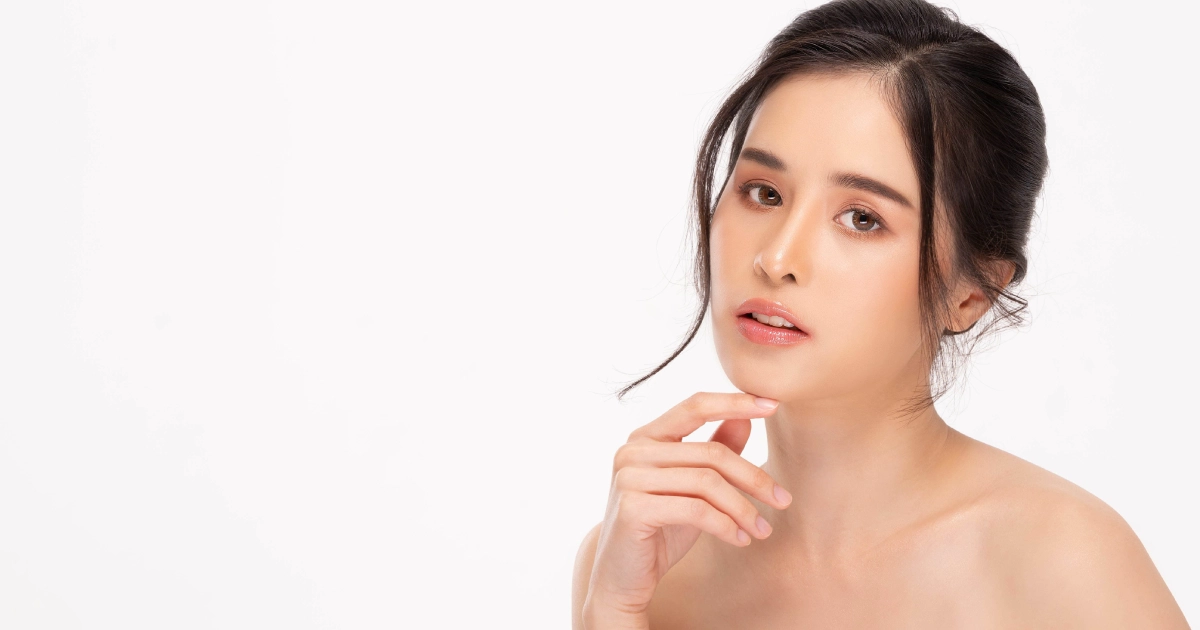 Studio portrait of a woman with glowing skin and natural makeup, touching her chin against a white background, representing SkinCeuticals in Beverly Hills, CA.